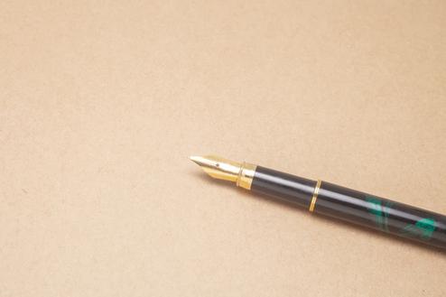 Nahaufnahme einer Füllfeder mit goldener Spitze auf einer braunen, strukturierten Unterlage.